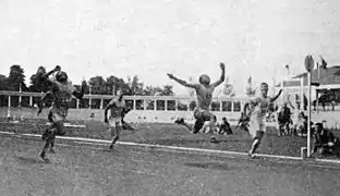 Photo de plusieurs hommes proches de franchir la ligne d'arrivée d'une course, l'un d'eux est en l'air après un saut.