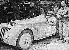 Photo d'un pilote prenant la pose dans une voiture avec à côté le copilote et la foule.