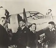 Photographie noir et banc avec les deux hommes devant l'avion en arrière-plan.