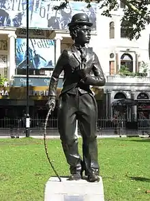 Statue en bronze de Charlot dans un parc devant un cinéma