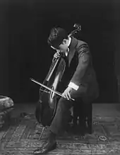 Chaplin, de profil et la tête en bas, assis sur un tabouret, jouant un violoncelle entre ses jambes