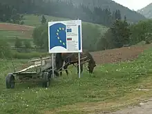 photographie couleurs : charrette à cheval derrière un panneau au logo européen