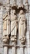 Trois statues contre des colonnes encastrées : une statue sans la tête, l'ange tourné vers Marie. Tous portent une toge.