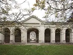 Vue d'une galerie à arcades s'ouvrant par un porche néoclassique.