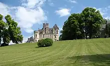 Photographie en couleurs d'un château en arrière-plan d'une vaste pelouse plantée d'arbres.