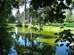 Photo en couleur d'un étang dans la verdure, un château se distinguant derrière les arbres