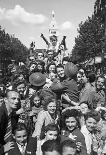 Sur l'avenue d'Orléans, foule de Parisiens en liesse accueillant les troupes britanniques, le 26 août 1944. En arrière-plan, dans l'axe de l'avenue, le clocher de l'église Saint-Pierre-de-Montrouge.