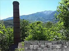 Cheminée de l'ancienne usine de grillage de minerai de fer. En médaillon : la raffinerie autrefois. Au fond : Pic du Canigou.