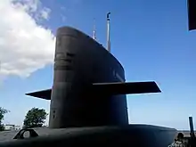Une forme verticale noire en contreplongée avec des ailerons sur le côté posée sur la coque du sous-marin