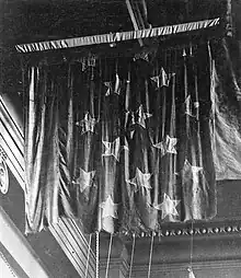 Photographie noir et blanc du drapeau de la Chesapeake attaché au plafond d'une pièce. Ses étoiles sont encore visibles malgré le fait qu'il soit déchiré sur son bas.