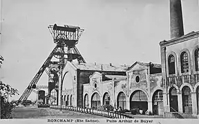 Photo noir et blanc de façades industrielles des années 1900 et grande tour triangulaire métallique à l'arrière plan.