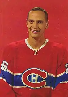 Photographie (portrait) couleur d’un homme portant un maillot de hockey sur glace rouge, devant un fond rouge