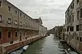 Canal étroit de Venise bordé de bâtiments sur les deux rives ; à gauche, l'église et l'hospice