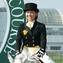 Femme de type asiatique souriant et chevauchant sa monture lors d'un concours