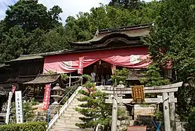 Bâtiment au sommet d'une volée d'escaliers modernes avec pignon vallonné de style chinois à l'avant. La partie inférieure est recouverte par un tissu rouge suspendu à l'avant-toit de la toiture.