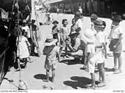 Photographie en noir et blanc d'un photographe accroupi encerclé d'une dizaine d'enfants.