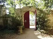Photographie en couleurs d'un espace végétalisé limité par des murs et un portail en bois.