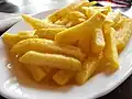 Tas de belles frites dorées et croustillantes sur une assiette blanche.