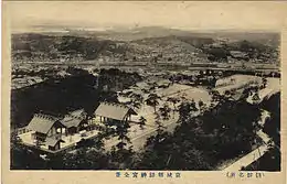 Photographie vue de loin d'un sanctuaire shinto. Plusieurs sont présents sur une colline, avec au loin une ville.