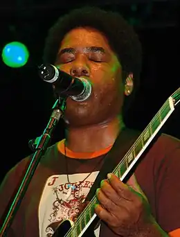 Photo en buste d'un guitariste noir jouant et chantant devant un micro