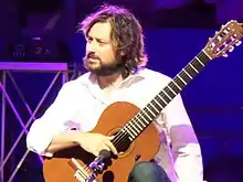 Photographie d'un homme assis sur scène, jouant de la guitare