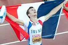 Lemaitre, les bras en l'air tendant un drapeau français dans son dos.