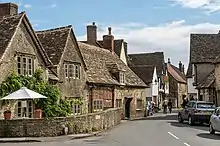 Petites maisons en pierres de couleur gris foncé séparées de la route goudronnée par un muret en pierres de la même couleur.