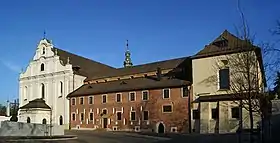 Photographie couleur d'une façade d'église baroque de pierre blanche, à gauche, et de bâtiments en briques à droite