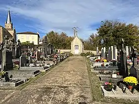 Une allée de cimetière bordée de tombes qui se termine sur une chapelle funéraire.