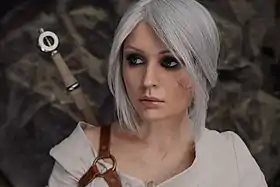 Photographie couleur d'une jeune fille aux cheveux argentés et à la peau pâle, une épée dans le dos.