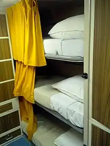 Trois couchettes superposées avec des rideaux jaunes.