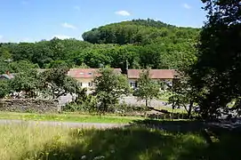 Groupe de maisons au pied d'une colline boisée.
