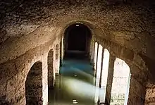 Vue intérieure d'une citerne avec des piliers en maçonnerie et de l'eau dans ses parties basses.