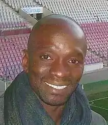 Épaules et visage d'un homme de face. Pose dans une tribune de stade, tribune opposée en arrière-plan.