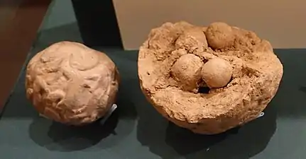 Deux bulles en argile avec des empreintes de sceaux, une complète et l'autre brisée, laissant apparaître des jetons ronds en argile.