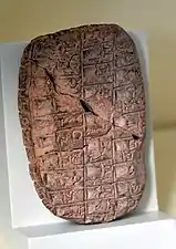 Tablette en argile ébréchée, divisée en cases comprenant des signes proto-cunéiformes et numériques.