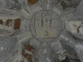 Photo en couleur d'une clef de voûte en pierre entre des briques formant nervures. La clef est sculptée d'un cercle contenant un château à trois tours.