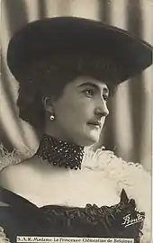 Photo de Clémentine en buste et en décolleté, arborant une immense capeline sombre coiffant ses cheveux relevés vers le haut et regardant à sa gauche