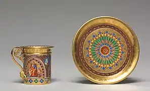 Une tasse et une sous-tasse dorées, à motifs de rois et encadrements géométriques très colorés.