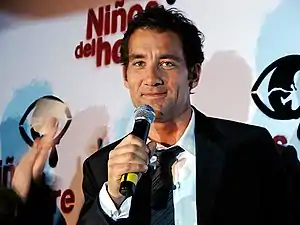Owen de face tenant un micro devant un logo en espagnol du film.