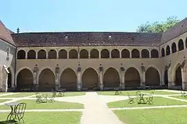 photographie en couleur d'un cloître avec de nombreuses colonnades sur deux niveaux ; au milieu, une pelouse avec des chemins en terre et des chaises en métal.