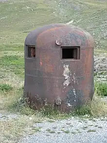 Photo d'un cuirassement bombé dépassant du béton, percé de plusieurs créneaux.