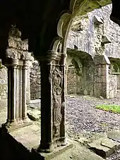 Photographie couleur d'une arcade ogivale de cloître, dont la colonne est sculptée, représentant un abbé tenant une crosse.