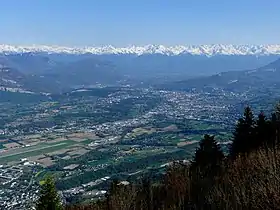 Vue de la cluse de Chambéry depuis le mont du Chat au nord avec Chambéry et son agglomération au centre, le massif des Bauges à gauche, le massif de la Chartreuse à droite et la chaîne de Belledonne enneigée par delà la combe de Savoie au loin.