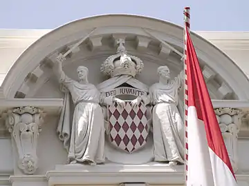 Haut-relief des armoiries inscrit dans le fronton circulaire au-dessus de l'entrée principale avec un drapeau de Monaco, en juin 2008.