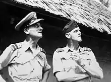 Photographie noir et blanc. Harry Cobby et Clive Caldwell en tenue militaire regardent le ciel. Derrière eux, se tient un bâtiment.
