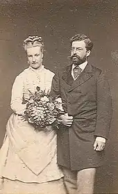 Portrait en pied de Louise vêtue d'une robe claire et tenant une gerbe de fleurs et de son mari revêtu d'une redingote sombre, barbe sombre et lorgnons.