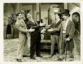 photographie en noir et blanc de quatre personnages souriants se tendant la main