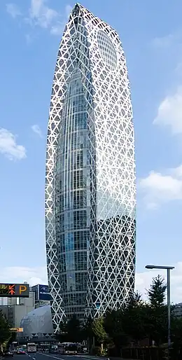 Ground-level view of a blue, glass high-rise. Two opposite sides of the building curve inward until meeting at the top; these sides also have many white stripes haphazardly strewn across them.