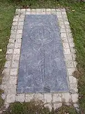 Photographie d'une dalle funéraire placée dans l'herbe.